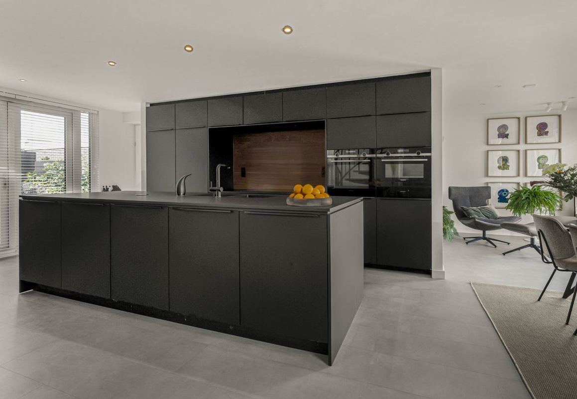 Open keuken met zwarte fronten en een kookeiland, met zicht op de woonkamer